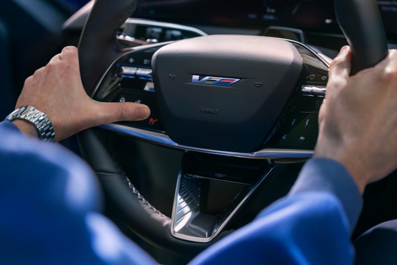 Close-up of a Man About to Press the V-Button on the 2026 OPTIQ-V Steering Wheel | Garlyn Shelton Cadillac in Temple TX